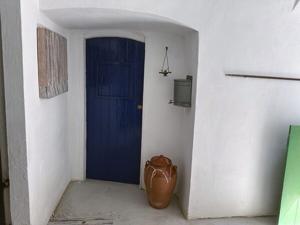 A hallway with a blue door, a wall-mounted light fixture, and a terracotta pot.