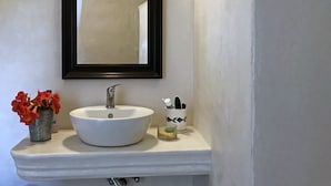 Ein Badezimmer mit einem weißen Waschbecken, einem Spiegel und einer kleinen Vase mit roten Blumen.