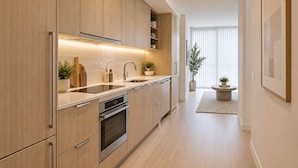 A modern kitchen with wooden cabinets, stainless steel appliances, and a central island with a sink. - Unionmark Suites (Toronto)