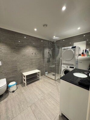 A modern bathroom with a glass-enclosed shower, a built-in washing machine, and a toilet with a trash bin. - Luxury 2-bedroom apartment in charming Vestland perfect for relaxing stay (Vestland)