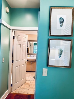 A hallway with teal walls, a white door, and a bathroom visible in the background.