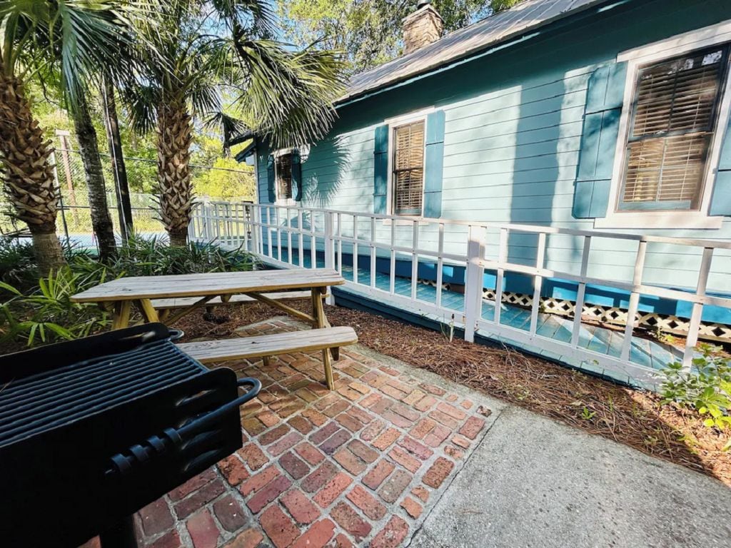 A patio area with a grill, picnic table, and a house with a white fence.