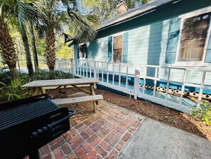 Eine Terrassenfläche mit Grill, Picknicktisch und einem Haus mit weißem Zaun.