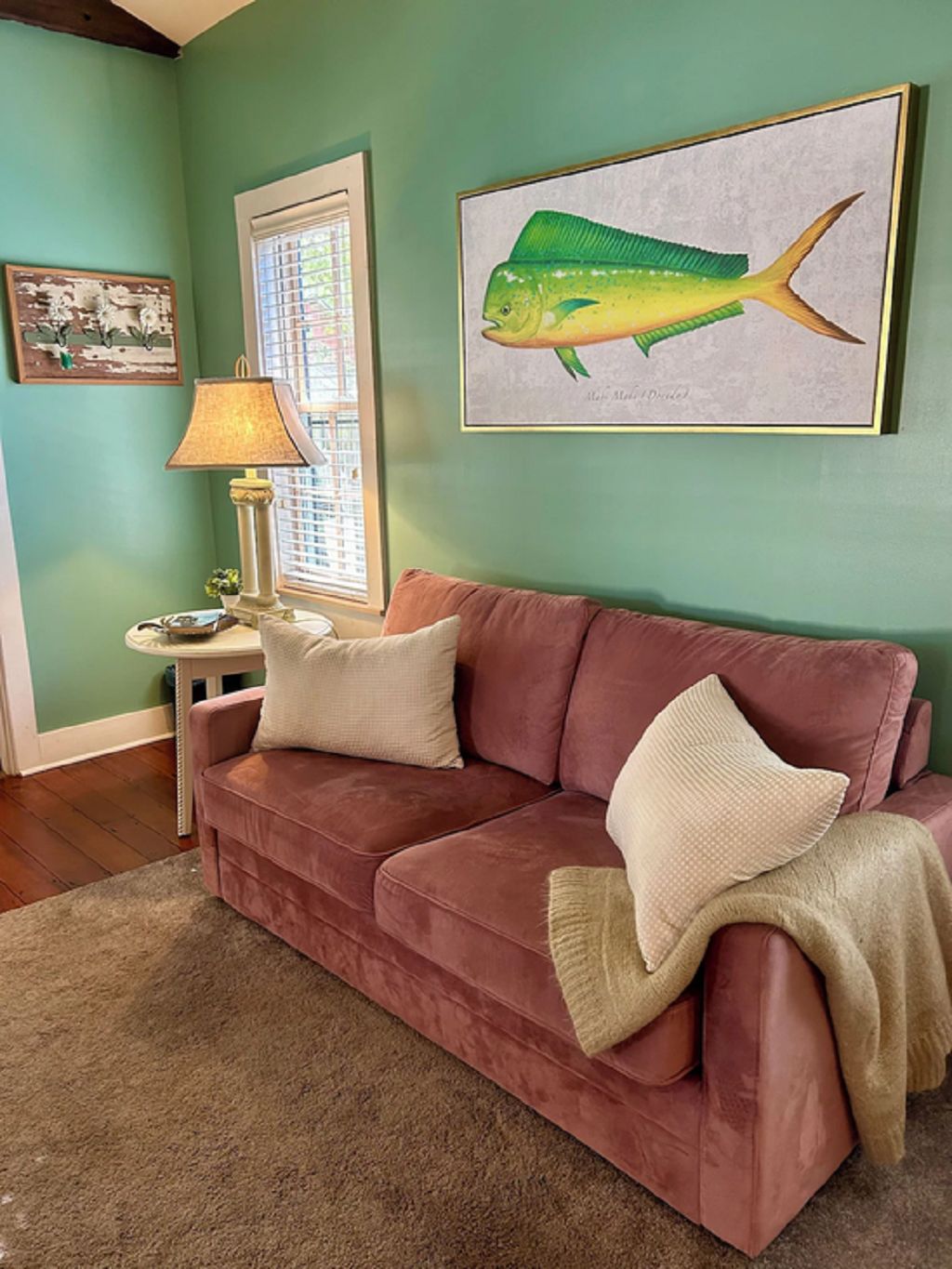 A room with a green wall, a red sofa, a lamp, and a framed fish painting.