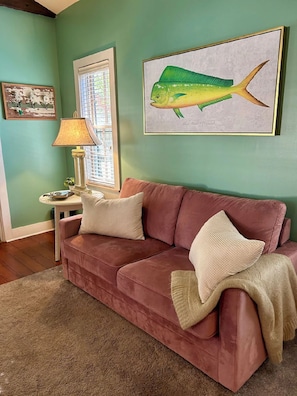 A room with a green wall, a red sofa, a lamp, and a framed fish painting.