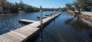 A wooden dock extending into calm water, surrounded by trees and a clear sky.