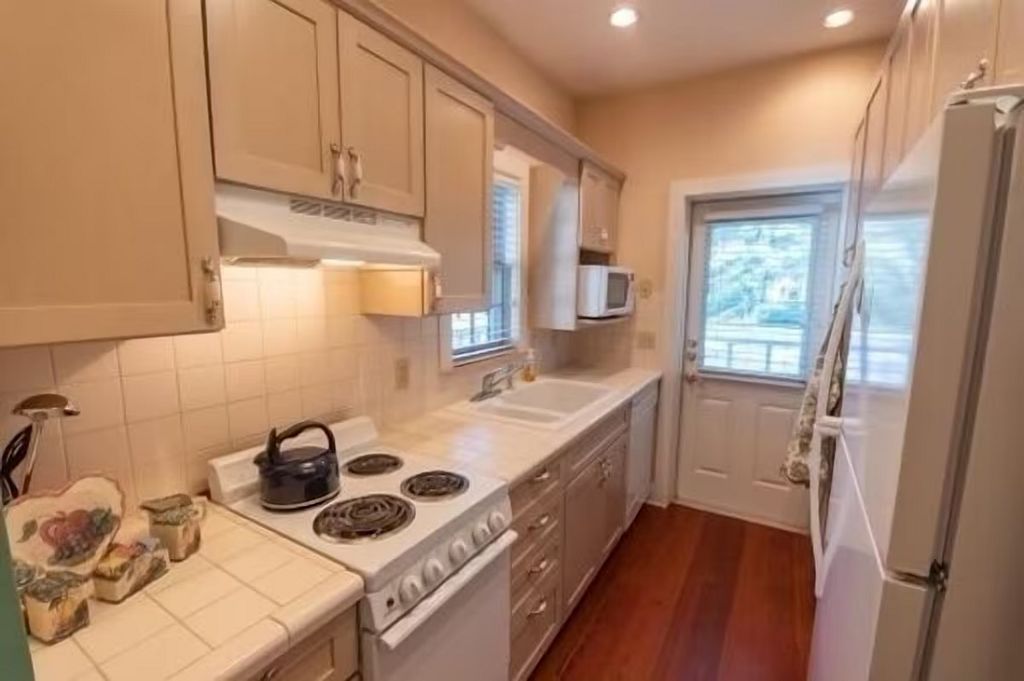 A kitchen with white cabinets, a stove, a microwave, and a refrigerator.