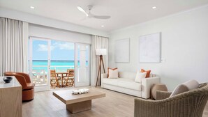 A modern living room with a large window, a sofa, a coffee table, and a wicker chair. - Oceanfront 1BR at Alexandra Resort Grace Bay Beach (The Bight Settlement)