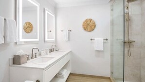 A modern bathroom with two sinks, a glass shower enclosure, and decorative wall mirrors. - Oceanfront 1BR at Alexandra Resort Grace Bay Beach (The Bight Settlement)