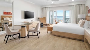 A hotel room with a bed, a TV, a dining table with chairs, a balcony with a view of the sea, and a ceiling fan. - Oceanfront 1BR at Alexandra Resort Grace Bay Beach (The Bight Settlement)