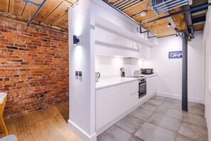 Eine moderne Küche mit weißen Schränken, einer Ziegelwand und freiliegenden Rohren an der Decke.
