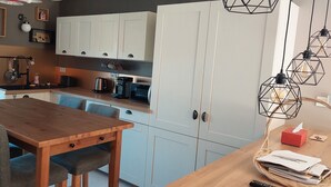 Une cuisine moderne avec des meubles blancs, une table à manger en bois et un panier rempli de papiers posé sur le comptoir.
