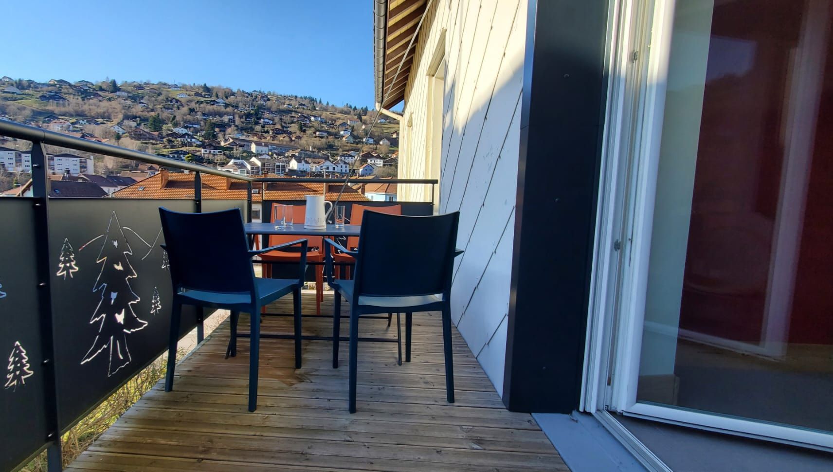 Un balcón con piso de madera, dos sillas y una mesa.