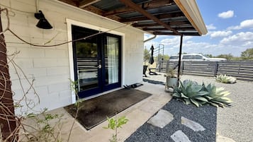 Um edifício residencial com varanda coberta, porta preta e caminho de cascalho que leva à entrada.