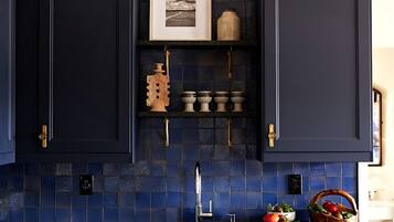 Cozinha com armários azul escuro, painel atrás do fogão em azulejos e uma pia.