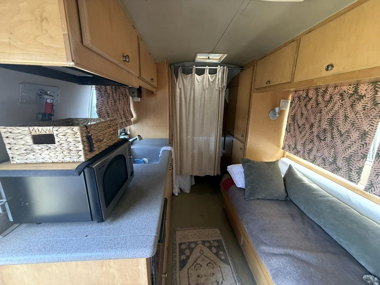 Un intérieur de camping-car compact comprenant un coin cuisine, un espace salon avec des coussins et une fenêtre avec des rideaux.