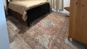 Une chambre à coucher avec un lit, une armoire en bois, un tapis à motifs et une fenêtre avec des rideaux.