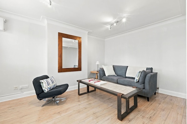 Ein modernes Wohnzimmer mit einem grauen Sofa, einem schwarzen Sessel, einem Holztisch und einem großen Spiegel an der Wand.