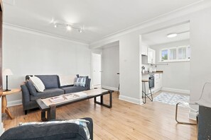 Ein modernes Wohnzimmer mit Sofa, Couchtisch und einer Küchenzeile im Hintergrund.