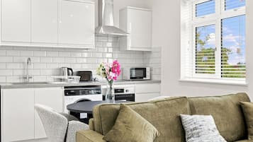 Eine moderne Küche mit weißen Schränken, einer Edelstahl-Dunstabzugshaube und einem Essbereich mit einem grünen Sofa und einer Blumenvase.