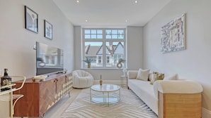 A modern living room with a sofa, a coffee table, a TV, and a window with a view of houses. - Luxury Apartment w/ Modern Kitchen & Free Parking (Southend-on-Sea)