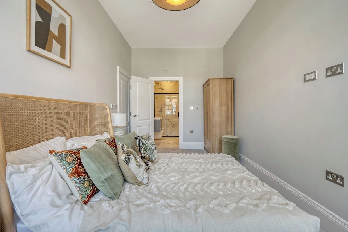 A bedroom with a bed, pillows, a headboard, a wardrobe, and a door leading to a bathroom.