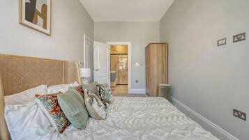 A bedroom with a bed, pillows, a headboard, a wardrobe, and a door leading to a bathroom.