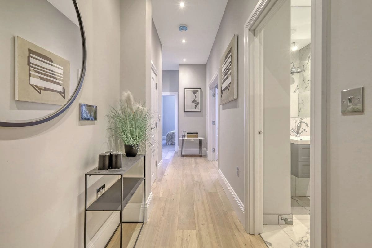 A hallway with a wooden floor, a potted plant, and framed artwork on the walls.