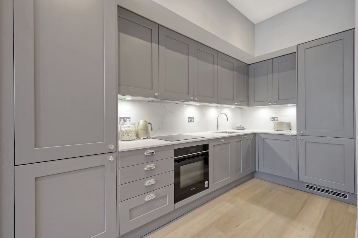 A modern kitchen with grey cabinetry, a built-in oven, and a countertop with a kettle and other items.