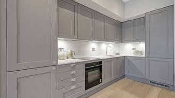 A modern kitchen with grey cabinetry, a built-in oven, and a countertop with a kettle and other items.