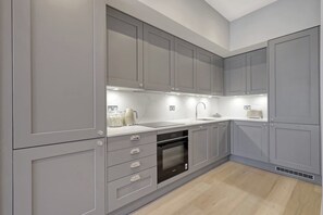 A modern kitchen with grey cabinetry, a built-in oven, and a countertop with a kettle and other items.