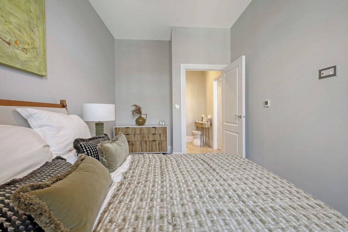 A bedroom with a bed, bedside table, lamp, and a door leading to a bathroom.