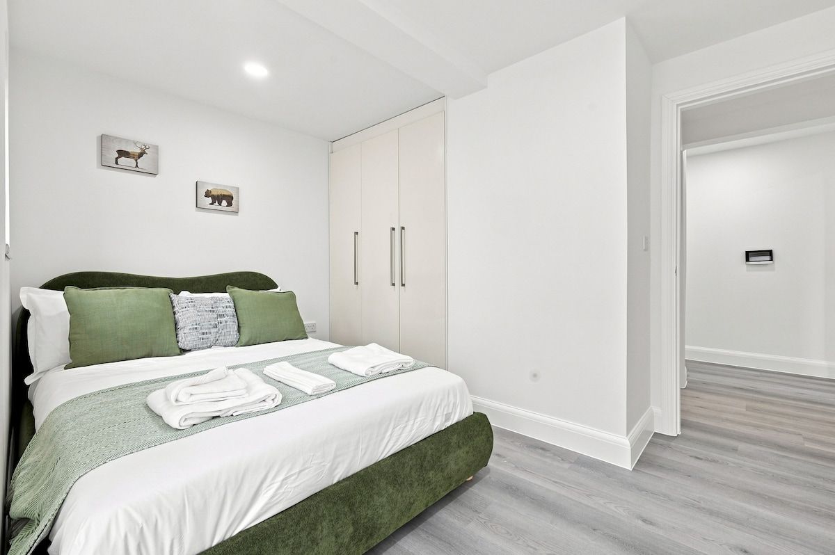 Ein Schlafzimmer mit einem Bett, grüner Bettwäsche, einem Kleiderschrank und zwei Wandbildern von Tieren.