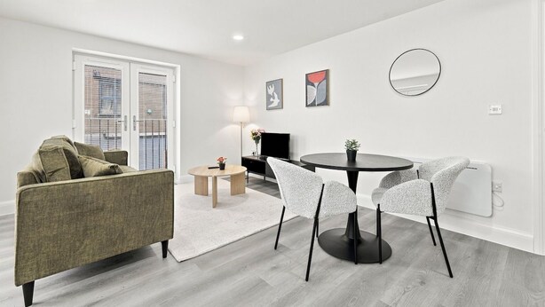 A modern living room with a sofa, a dining table with chairs, a TV, and artwork on the wall.