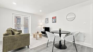 Un salon moderne avec un canapé, une table à manger et des chaises, un téléviseur et des œuvres d’art accrochées au mur.