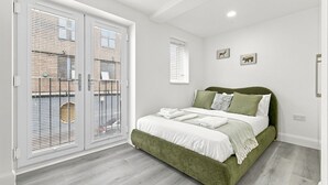 A bedroom with a green upholstered bed, white bedding, and a large window with blinds.