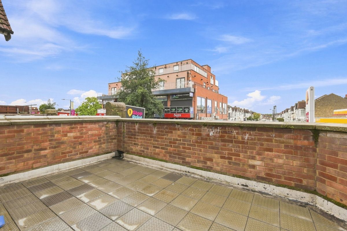 A brick wall with a tiled floor, a bus stop, and a building in the background.