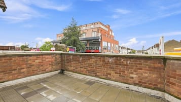 A brick wall with a tiled floor, a bus stop, and a building in the background.