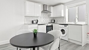 A modern kitchen with white cabinetry, a black countertop, and a round dining table with chairs.