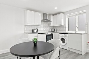 A modern kitchen with white cabinetry, a black countertop, and a round dining table with chairs.