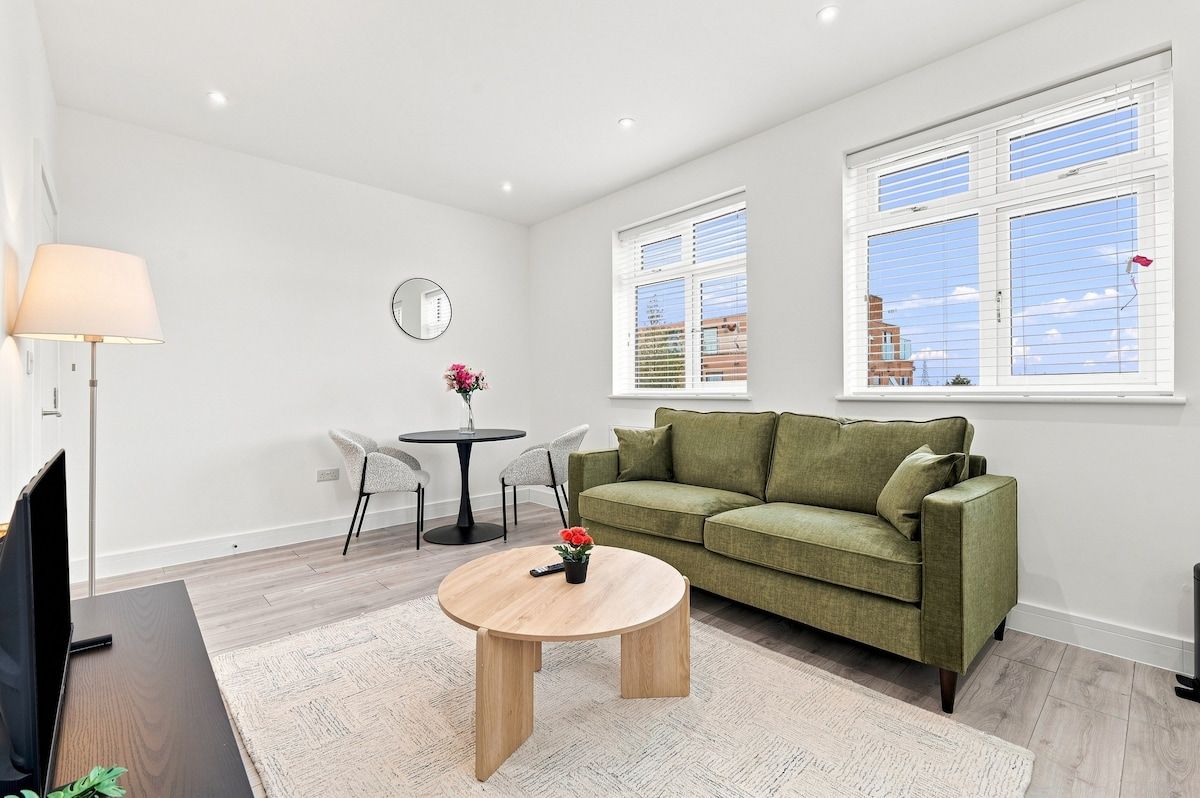 Un salon moderne avec un canapé vert, une table basse ronde et un coin repas comprenant une petite table et des chaises.