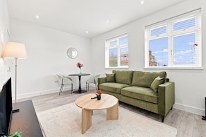 Un salon moderne avec un canapé vert, une table basse ronde et un coin repas comprenant une petite table et des chaises.