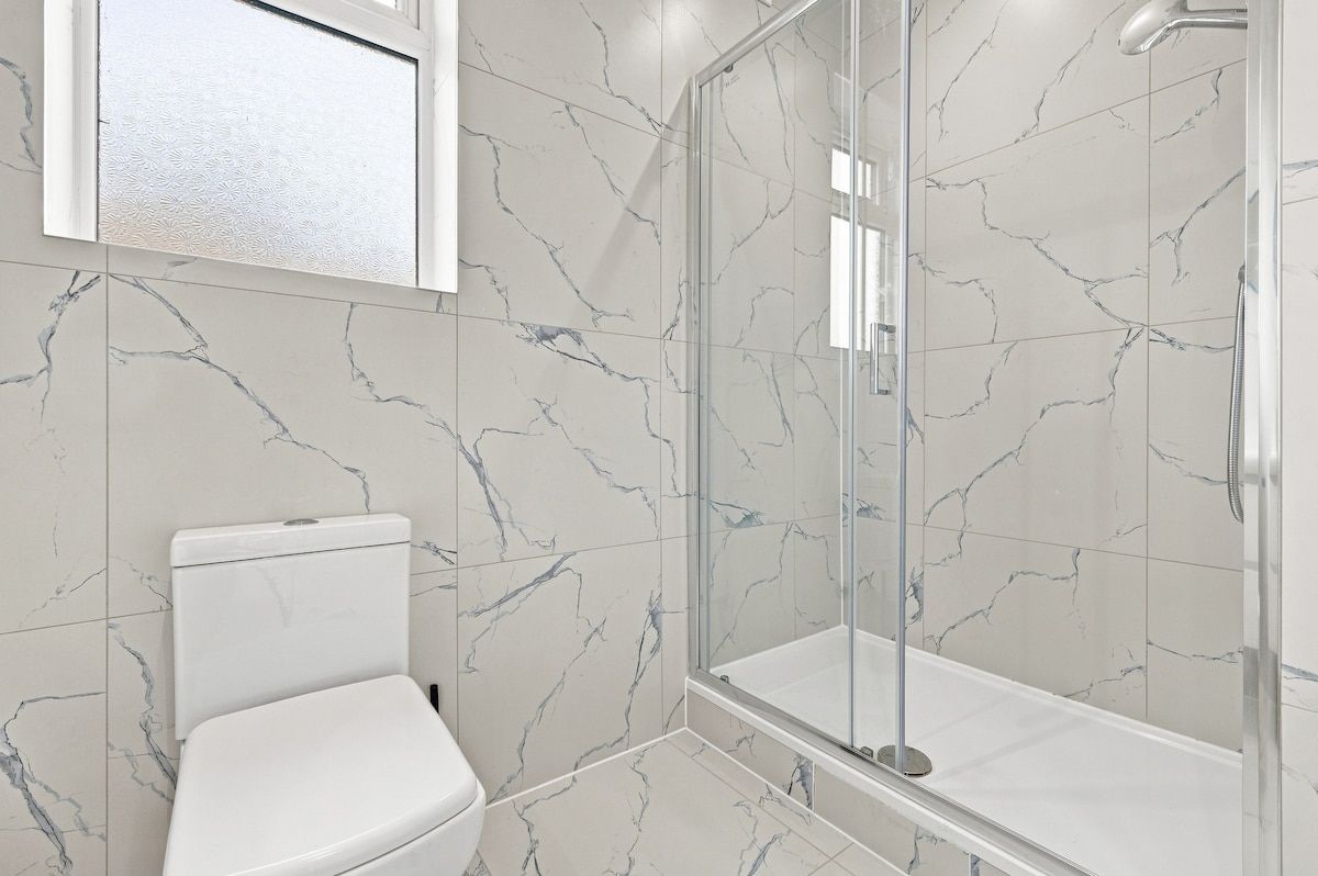 A bathroom with a toilet, a glass-enclosed shower, and marble-patterned walls.