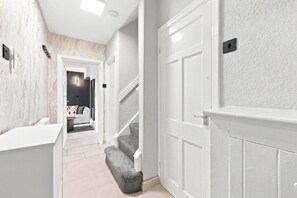 A hallway with a staircase leading to a living area, white walls, and a marble-like textured wall on one side. - Entire 5 Bed house in Manchester, UK (Withington)