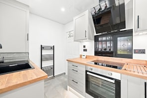 A modern kitchen with white cabinetry, a wooden countertop, a built-in oven, and a stainless steel range hood. - Entire 5 Bed house in Manchester, UK (Withington)