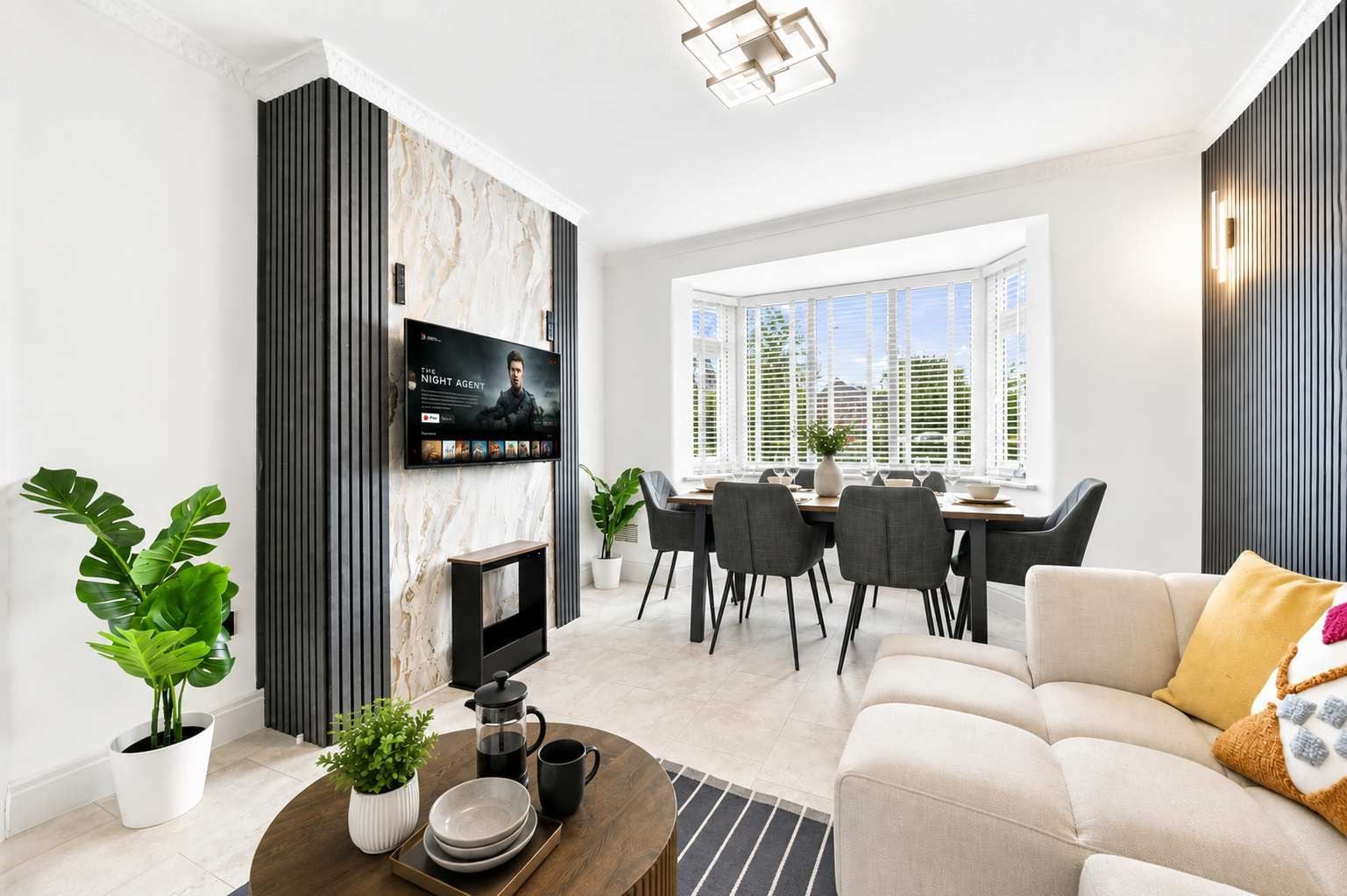 A modern living room with a flat-screen TV, a dining area with a table and chairs, and a sofa with a decorative pillow.