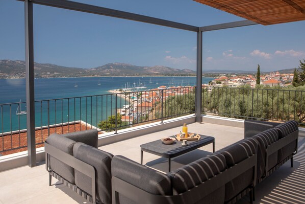 A balcony with a view of the sea, a dining area with a table and chairs, and a sofa.