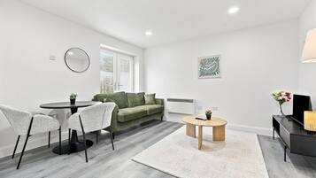 Un salon moderne avec une table à manger ronde, un canapé vert et un meuble pour la télévision avec une lampe.