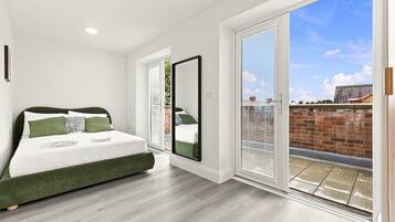 Une chambre à coucher comprenant un lit, un grand miroir et une porte-fenêtre coulissante donnant sur un espace extérieur.