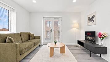 Un salon avec un canapé, une table basse, un téléviseur posé sur un meuble et une lampe.